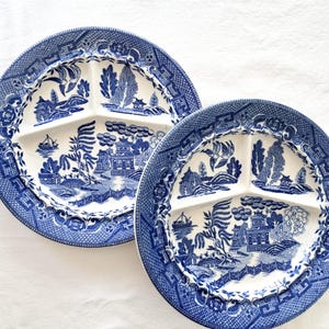 May include: Two blue and white divided plates with a classic Willow pattern. Each plate has three sections and a detailed border. The plates feature a scenic design with pagodas, trees, and a boat.