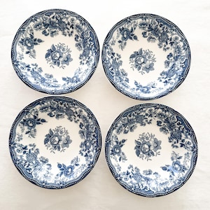 May include: Four white ceramic bowls with a blue floral pattern. Each bowl features a central floral design and a detailed border. The rims have a scalloped edge. The bowls are arranged on a white surface.