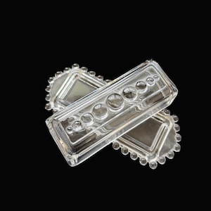 May include: Two clear glass rectangular dishes with decorative bubble and bead details. The dishes are stacked at an angle against a black background. The dishes have a rectangular shape with rounded corners and a series of bubbles and beads.