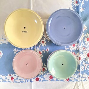 May include: Four ceramic bowls in different colors and sizes. The bowls are arranged on a white tablecloth with a floral pattern. The bowls are labeled A, B, C, and D. Bowl B is labeled "SOLD".