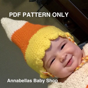 May include: A crochet candy corn hat in white, orange, and yellow. The hat is worn by a baby. The text "PDF PATTERN ONLY" is at the top of the image. The text "Annabellas Baby Shop" is at the bottom of the image.
