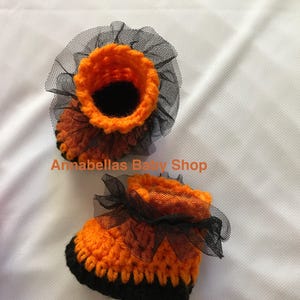 May include: A pair of orange and black crocheted baby booties with black tulle ruffles.  Annabellas Baby Shop.