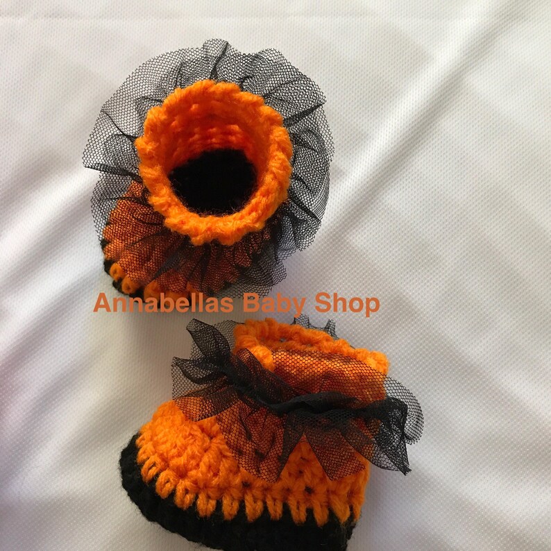 May include: A pair of orange and black crocheted baby booties with black tulle ruffles.  Annabellas Baby Shop.