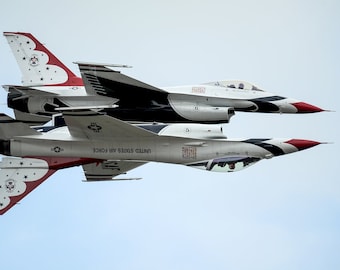 Peut inclure: Deux avions de chasse F-16 Fighting Falcon de l'US Air Force volent en formation, l'un à l'envers au-dessus de l'autre. Les deux avions sont peints dans un schéma de couleurs blanc, rouge et noir avec des étoiles sur la queue.