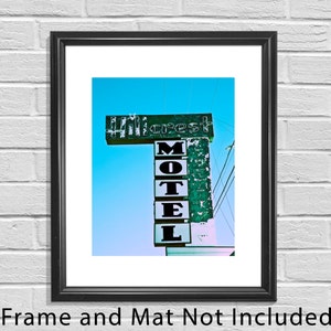 May include: A vintage motel sign with the words "Motel" and "Hillcrest" in white letters on a green background. The sign is weathered and faded, with some of the letters missing. The sign is against a bright blue sky.
