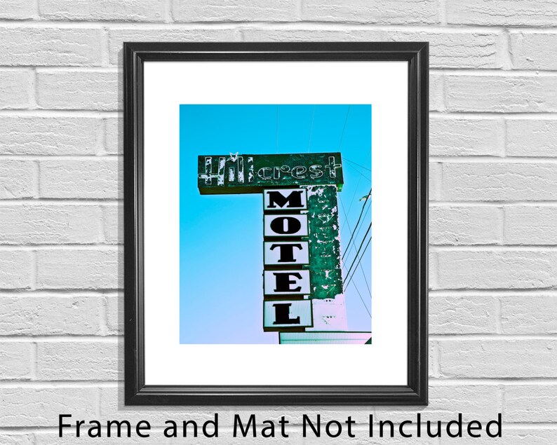May include: A vintage motel sign with the words "Motel" and "Hillcrest" in white letters on a green background. The sign is weathered and faded, with some of the letters missing. The sign is against a bright blue sky.