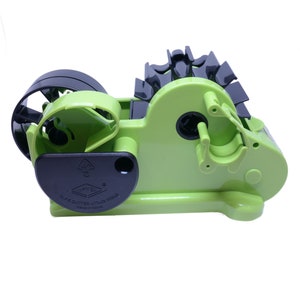 May include: A green and black tape dispenser with a clear tape roll. The dispenser has a black handle and a black label that says "D-C Tape Cutter, Japan Made, Made in China".
