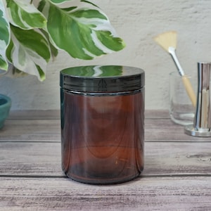 May include: A brown glass jar with a black lid. The jar is empty and has a smooth, rounded shape.