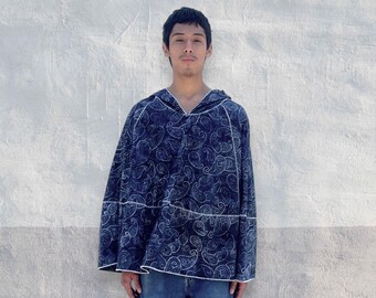 Könnte beinhalten: Ein dunkelblauer Kapuzenponcho mit einem durchgehenden weißen Paisleymuster. Das Kleidungsstück hat eine lockere, weit geschnittene Silhouette mit sichtbaren weißen Nähten entlang der Säume, kombiniert mit einer einfachen blauen Jeans.