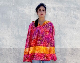 Könnte beinhalten: Ein Kapuzenponcho mit einem lebendigen Muster aus rosa, violetten und orangefarbenen Sternen. Das Kleidungsstück verfügt über ein horizontales Band aus einfarbigem orangefarbenem und gelbem Stoff im Mittelteil sowie eine lockere, fließende Passform.