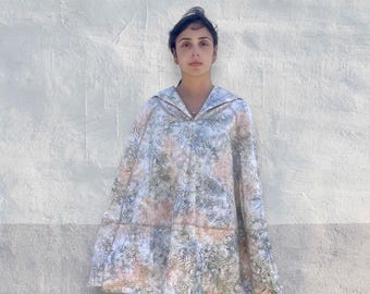 Könnte beinhalten: Ein ärmelloser Poncho mit einem dezenten Blumenmuster in Salbeigrün, Altrosa und Schieferblau. Das Kleidungsstück hat einen breiten, umgeschlagenen Kragen, der einen V-Ausschnitt bildet, und eine lockere, ausgestellte Form bis zur Mitte der Oberschenkel.