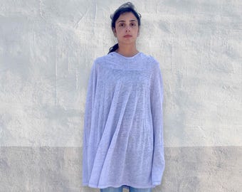 Könnte beinhalten: Ein helllavendelfarbenes, locker sitzendes Langarmshirt mit Rundhalsausschnitt und halbtransparentem, strukturiertem Stoff. Das Kleidungsstück hat eine entspannte, fließende Silhouette, die über den Oberkörper fällt, kombiniert mit einer klassischen blauen Jeans.