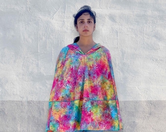 Könnte beinhalten: Ein Kapuzenponcho mit einem leuchtenden, mehrfarbigen Batikmuster in wirbelnden Rosa-, Blau-, Gelb- und Grüntönen. Das Kleidungsstück hat eine lockere, fließende Silhouette mit einer horizontalen Naht in der Mitte und einem blauen Saum.
