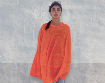 Könnte beinhalten: Ein leuchtend orangefarbener, locker sitzender Poncho mit langen Ärmeln, Rundhalsausschnitt und einer halbtransparenten, strukturierten Stoffoberfläche. Das Kleidungsstück hat eine weite, fließende Silhouette und wird mit einer blauen Jeans kombiniert.