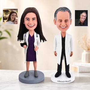 May include: Two custom bobblehead figurines depicting medical professionals. The left figure has long brown hair, a white lab coat, a purple dress, and a stethoscope. The right figure has short grey hair, a white lab coat, black shirt, and black trousers, with the text inReach Health on the base.