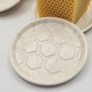 Peut inclure: Un plat en céramique blanche avec un motif en nid d'abeille. Le plat est fait d'un matériau moucheté et a un bord surélevé.