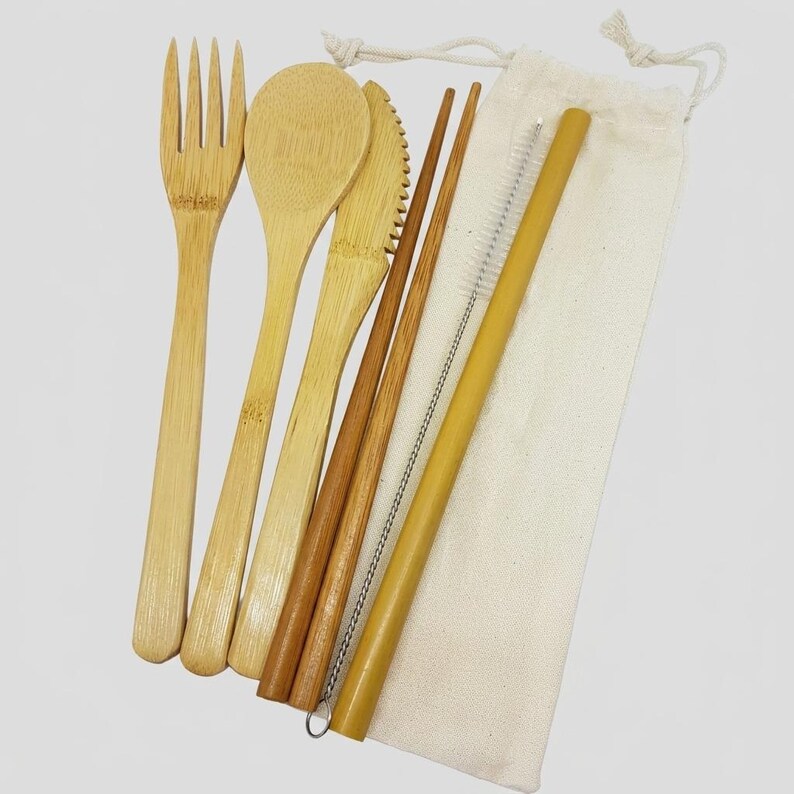 May include: A bamboo cutlery set including a fork, a spoon, a serrated knife, two chopsticks, and a straw with a cleaning brush, all stored in a light beige drawstring fabric pouch. The utensils are light brown with a natural wood grain finish.