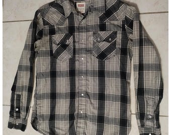 May include: A long-sleeved plaid shirt in black, gray, and white. The shirt has two chest pockets, a button-down front, and buttoned cuffs. The Levi's brand label is visible on the shirt.