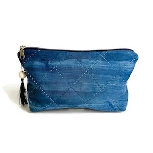 May include: A rectangular zippered pouch featuring a blue watercolor-style pattern with a diamond-shaped quilted stitch design. The zipper pull is adorned with a small wooden bead and a black fabric tassel attached to the silver metal hardware.