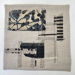 May include: A beige linen cushion with a black and white abstract design created with stitched fabric scraps. The design features geometric shapes and a floral pattern.