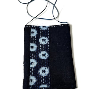 May include: A small black fabric bag with a blue and white patterned fabric panel and a blue beaded fringe. The bag has a long black strap.
