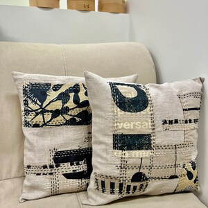 May include: Two decorative throw pillows with a beige linen fabric and black and white geometric patterns. The pillows are on a beige couch.