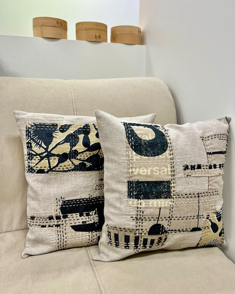 May include: Two decorative throw pillows with a beige linen fabric and black and white geometric patterns. The pillows are on a beige couch.