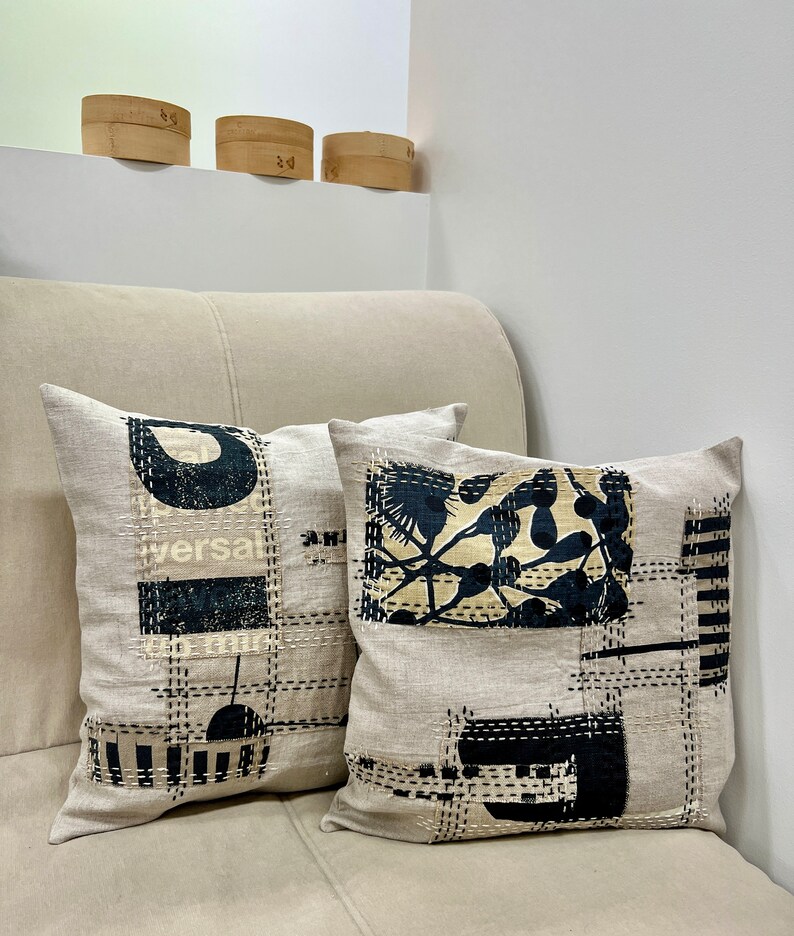 May include: Two decorative throw pillows with black and white geometric designs on a beige linen fabric. The pillows are sitting on a beige couch.
