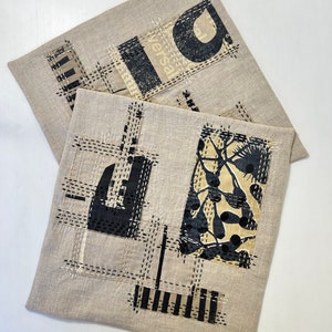 May include: Two beige linen pillow covers with black and white geometric designs. One cover features a black and white floral pattern, while the other has a black and white geometric pattern with the word "Versal" visible.