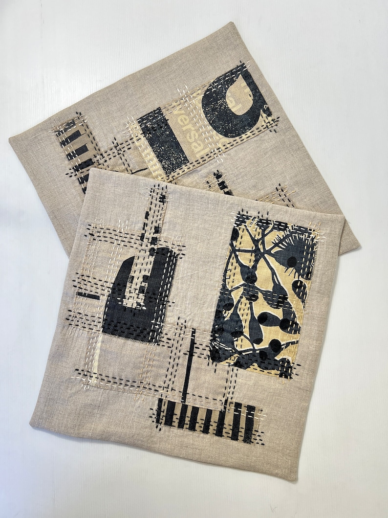 May include: Two beige linen pillow covers with black and white geometric designs. One cover features a black and white floral pattern, while the other has a black and white geometric pattern with the word "Versal" visible.