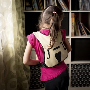 Puede incluir: Una persona joven que lleva una camisa rosa y pantalones negros con una mochila con forma de violín blanca y negra.