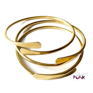 May include: Three gold-toned metal bangles with a slightly curved, flat edge. The bangles are stacked on top of each other.