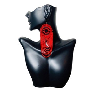 May include: A pair of long, red beaded earrings with a black beaded circle design at the top.