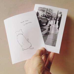 May include: A white card with black ink that says "Your dog is waiting..." and a line drawing of a dog. The card is held in a hand, and a black and white photo of a dog on a sidewalk is visible in the background.