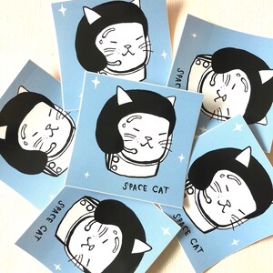 K&ouml;nnte beinhalten: Sechs blaue und wei&szlig;e illustrierte Karten mit dem Text "Space Cat" auf jeder Karte. Jede Karte zeigt eine Schwarzwei&szlig;illustration einer Katze mit einem Weltraumhelm.