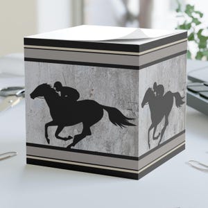 May include: A gray and black cube-shaped notepad with a silhouette of a horse and rider on a gray background. The notepad has a black and gray striped border.