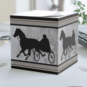 Peut inclure: Un bloc-notes gris et noir avec une silhouette de cheval et de conducteur de course sur un fond de béton. Le bloc-notes a une bordure rayée noire et blanche.