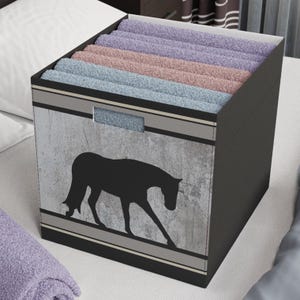 May include: A black storage box with a gray and white horse silhouette design. The box is filled with folded towels in shades of blue, purple, and pink.