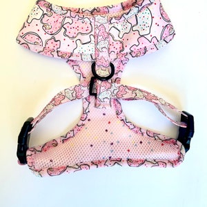 May include: Pink dog harness with a cookie pattern. The harness has a mesh lining and adjustable straps with black buckles.