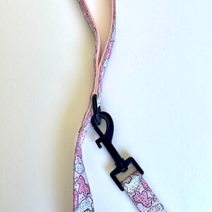 May include: Pink dog leash with a black clip and a pattern of pink and white cookies.