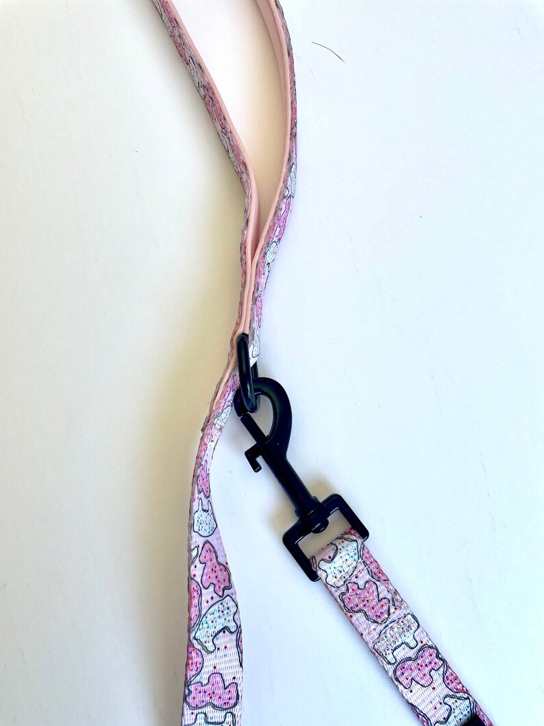 May include: Pink dog leash with a black clip and a pattern of pink and white cookies.
