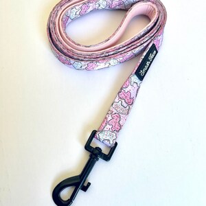 May include: Pink dog leash with a white background and a pattern of pink and white cookies. The leash has a black clip and the text "Smash Face" is printed on the leash.