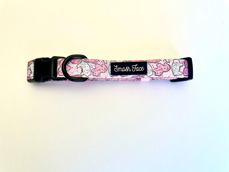 May include: A pink and white dog collar with a black buckle and a white label that says "Smash Face".