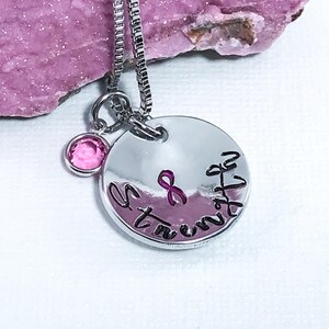 May include: Silver necklace with a round pendant that says "Strength" with a pink ribbon and a pink crystal charm.