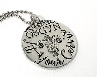May include: Silver necklace with a round pendant that says "OBGYN At Your Cervix" with a stylized uterus design in the center.