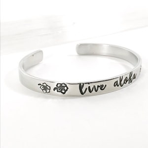 May include: Silver bangle bracelet with the words "Live Aloha" engraved on it. Two small flower designs are engraved on either side of the text.