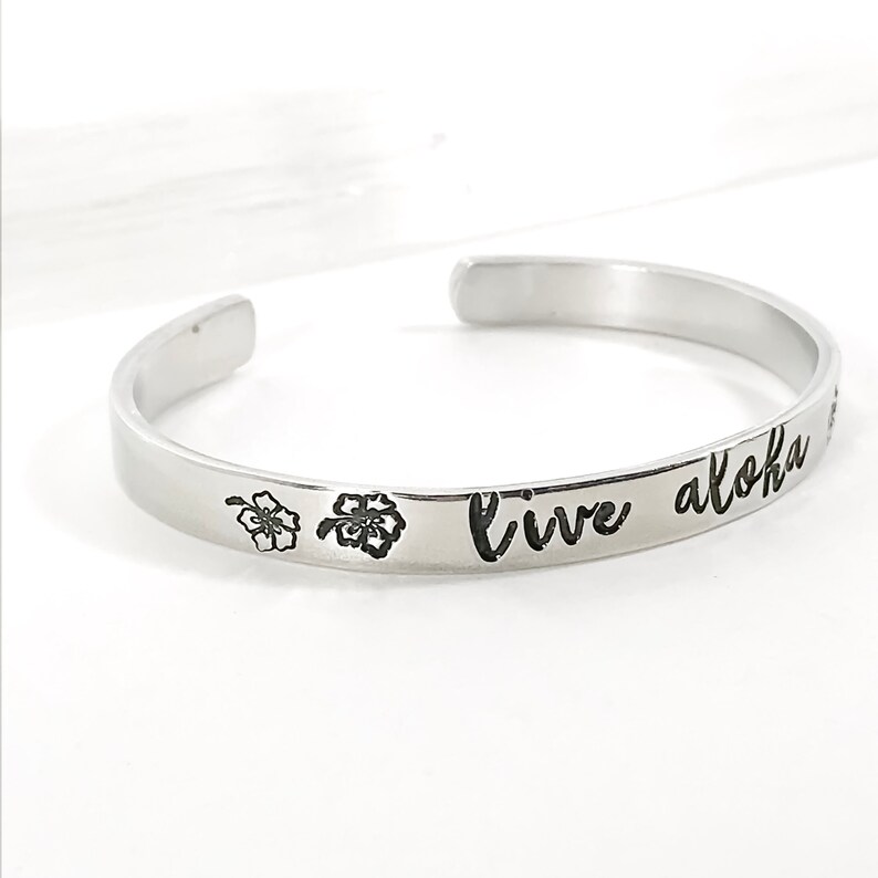 May include: Silver bangle bracelet with the words "Live Aloha" engraved on it. Two small flower designs are engraved on either side of the text.