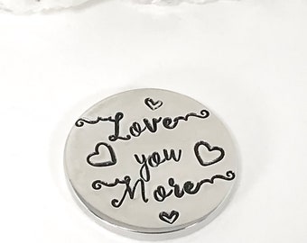 May include: Silver charm with the text "Love you more" and hearts.