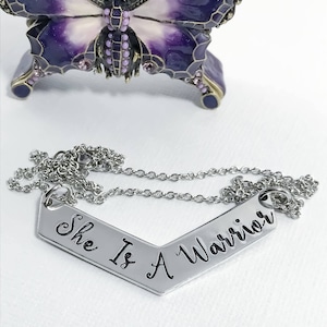 May include: Silver necklace with a chevron-shaped pendant that reads "She Is A Warrior".