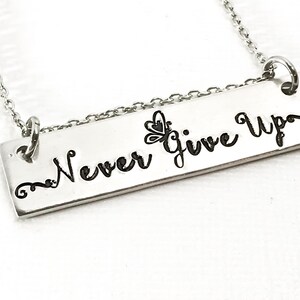 May include: Silver necklace with a rectangular pendant that says "Never Give Up" with a small butterfly design above the words.